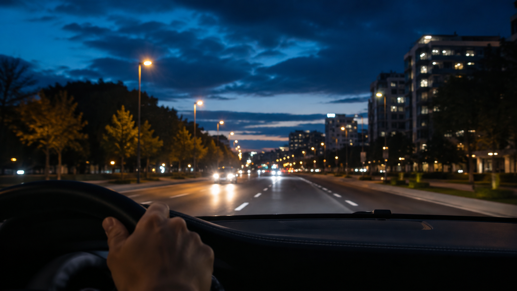 Vista do interior de um carro ao anoitecer, com a estrada e pontos de luz ao fundo.