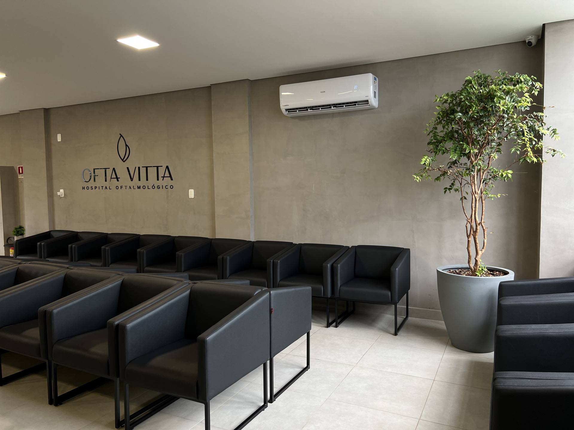 Sala de espera principal OFTA VITTA, poltronas pretas e logo na parede